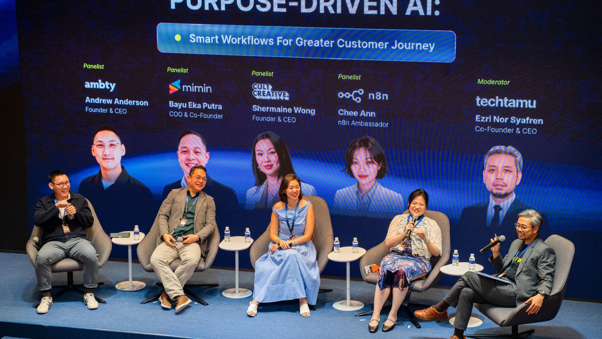 Chee Ann speaking into a microphone on a five-person conference panel, the stage screen behind reading Purpose-Driven AI