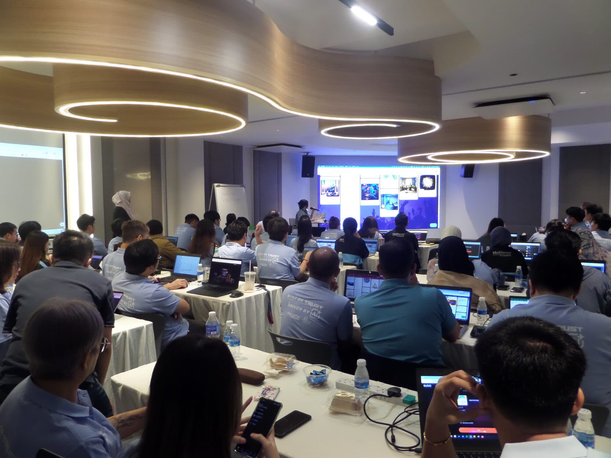 Participants working on laptops in a training room while the trainer presents at the front screen